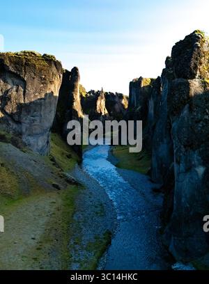 Serene view of a canyon in Iceland featuring rugged cliffs and a winding river. Bright sunlight illuminates the unique rock formations, creating a captivating outdoor experience. Stock Photo