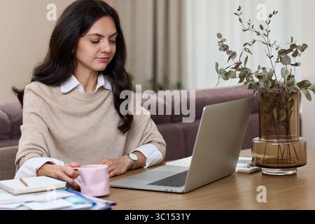 Happy positive woman using laptop while working remotely from home in living room, success freelance entrepreneur or remote work concep Stock Photo
