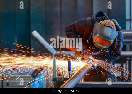Germany - Theme photo: Metal industry. An industrial worker cuts a steel pipe with an angle grinder. Stock Photo