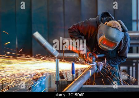Germany - Theme photo: Metal industry. An industrial worker cuts a steel pipe with an angle grinder. Stock Photo