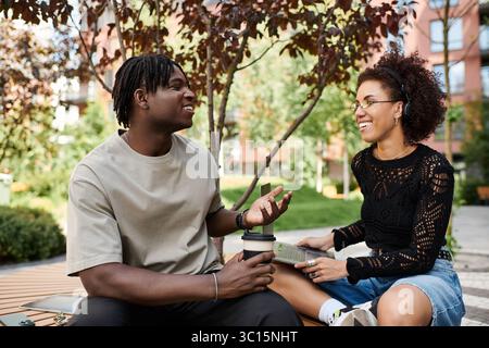 A young African American couple engaged in remote work at a city park on a sunny summer day. Stock Photo