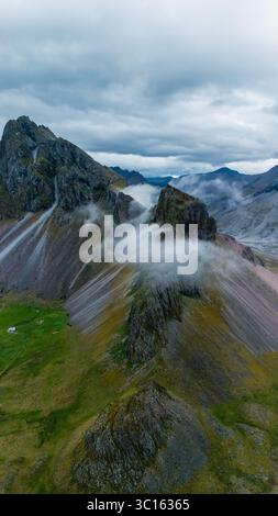 Breathtaking Icelandic landscape featuring rugged mountains shrouded in clouds. The scene captures the wild beauty of nature, showcasing vibrant greenery at the base, a perfect backdrop for adventure. Stock Photo