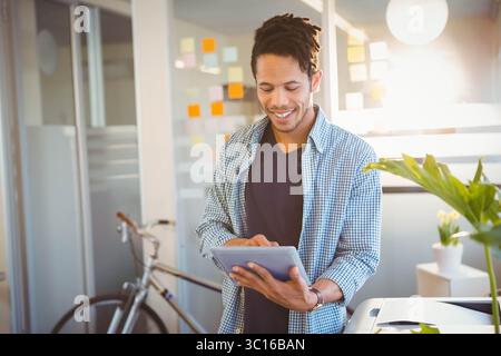 African American male tapping tablet near glass partition with sticky notes and bicycle in office Stock Photo