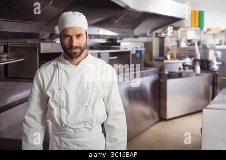 Male chef wearing white jacket apron and skullcap cutting vegetables on stainless steel prep table Stock Photo