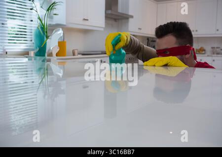Man scrubbing white countertop island in modern kitchen with green sponge and yellow gloves Stock Photo