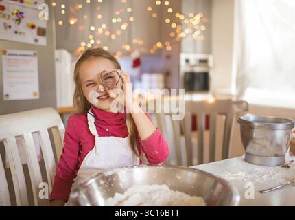 Child girl holding cookie cutter over eye mixing flour in bowl on table at home kitchen Stock Photo