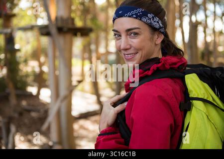 Female hiker standing on trail wearing red jacket, blue bandana, carrying green backpack near ropes Stock Photo