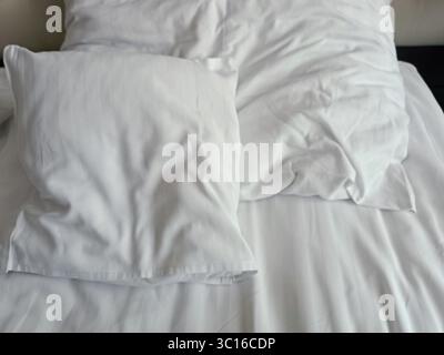 Empty wrinkled white bedding, close up, hotel, white pillows Stock Photo