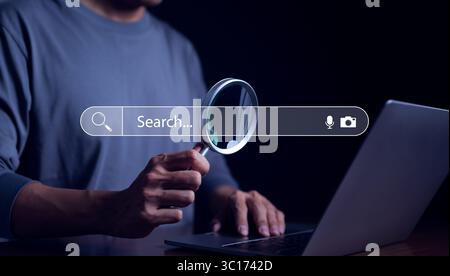 Search engine technology concept, Businessman holding magnifying glass and using laptop computer to Searching for internet information with web browse Stock Photo