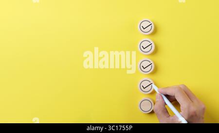 Checklist concept. Person using a black ink pen to correct sign and tick check mark on wooden block with copy space for the checklist Stock Photo