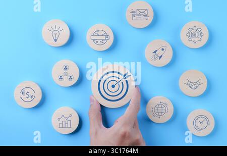 The concept of business goal and marketing target. Man hand holding wooden block with bullseye icon and other business icons. Goal objective strategy Stock Photo