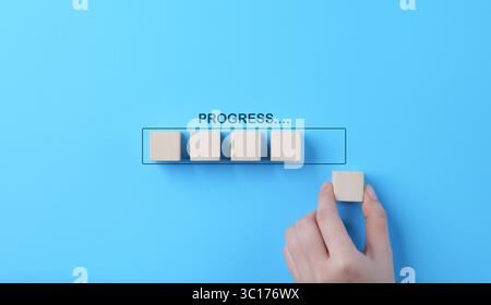 Hand places wooden cubes arranged in row on blue background. with the word progress. in progress, work loading bar, achievement business project plan, Stock Photo