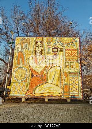Almaty, Kazakhstan - March 19, 2025: Vibrant mosaic artwork features a woman holding an object in an outdoor setting Stock Photo