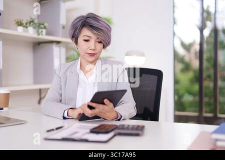 Experienced Asian professional focused on tablet screen in contemporary office managing data and digital communications Efficient workflow Stock Photo