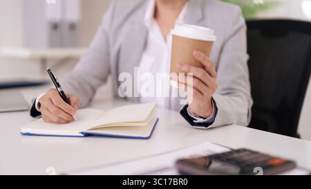 Adult professional engaged in detailed note taking within an organized office environment. Concentrated on work tasks planning and preparing for next Stock Photo