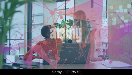 Collaborating office colleagues discussing project at office desk, with laptop and network overlay Stock Photo