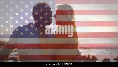 Embracing mature woman and senior man standing on rocky beach at sunset, wearing sweaters Stock Photo