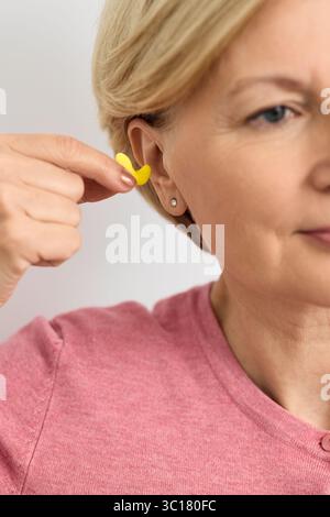 Individual earplugs for human. Woman holding individual yellow earplug near ear, close-up Stock Photo
