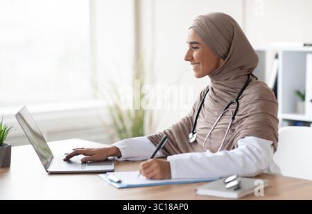 Young female doctor having online training, sitting in her cabinet Stock Photo