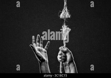 Hold on to Frayed Rope About to Break Asking for Help Against Textured Black Background Stock Photo