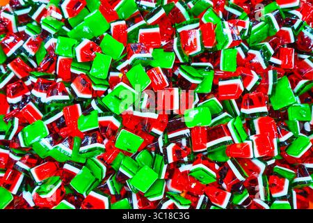 A vibrant pile of watermelon-themed jelly candies, featuring glossy red, green, and white layers in cube and wedge shapes Stock Photo