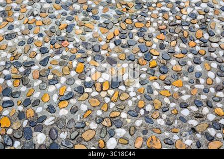 A detailed view of a decorative pebble stone pavement made from mixed colored pebbles set in concrete, used for walkways or garden paths Stock Photo