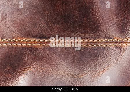 Brown leather texture closeup. Visible orange thread seam. Natural wrinkles and grain. Material surface detail. Handmade craftsmanship. Stock Photo