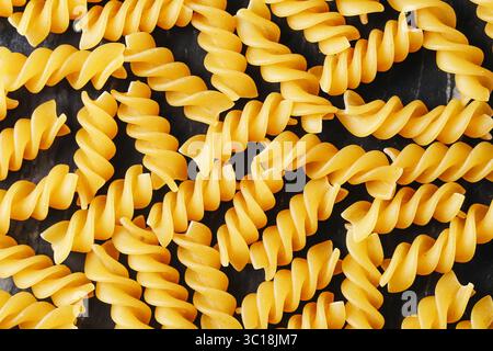 Yellow fusilli pasta background. Uncooked spiral noodles closeup. Italian raw food texture. Dry macaroni surface detail. Traditional ingredient. Stock Photo