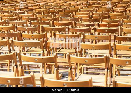 Many wooden chairs arranged in rows. Outdoor seating preparation for event. Brown folding chairs on pavement. Repetition and pattern. Stock Photo
