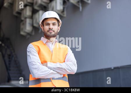 A construction worker stands confidently with arms crossed, wearing safety gear and a hard hat. Stock Photo
