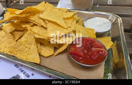 A classic appetizer of crispy tortilla chips (nachos) served on a platter with bowls of fresh tomato salsa and a creamy white dip for sharing. Stock Photo