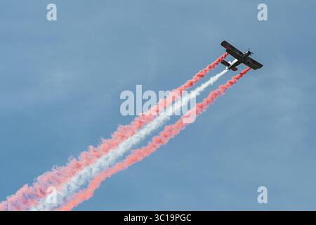 Old model of military aircraft performing in the sky emitting smoke in the colors of the Latvian flag during a military parade Stock Photo