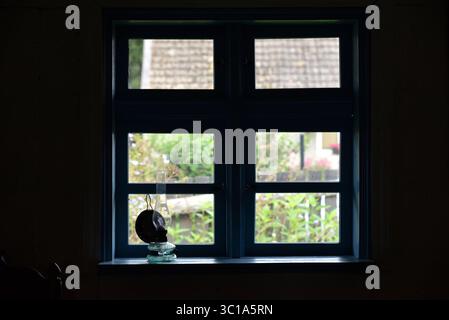 An old glass kerosene lamp sits on a blue windowsill with a view of a blurry green garden. Stock Photo