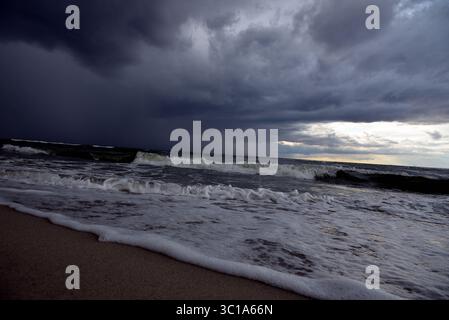 Dramatic seascape with dark storm clouds over the turbulent Baltic Sea on a sandy beach. Stock Photo