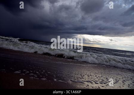 Dramatic seascape with dark storm clouds over the turbulent Baltic Sea on a sandy beach. Stock Photo