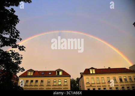 A vibrant rainbow arches over the rooftops of old apartment buildings in a German city after a summer rain shower. Stock Photo