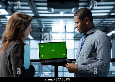 Engineer in data center using green screen laptop, refining server virtualization strategies, configuring cluster nodes, adjusting routing rules, maintaining efficient workflows Stock Photo