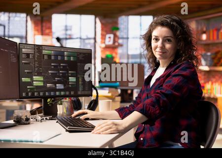 Portrait of smiling woman working in AI tech agency providing custom software development services. Upbeat IT staff member using machine learning to streamline coding process in startup office Stock Photo