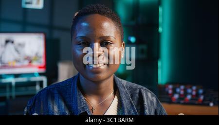 Portrait of jolly woman sitting on chair at home office desk in neon illuminated apartment late at night. Cheerful person in RGB lit living room enjoying leisure time, camera B Stock Photo