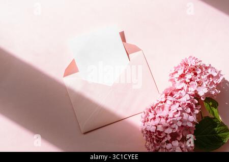Pink envelope with blank card and hydrangea flowers on pastel background. Top view, flat lay, mockup. Stock Photo