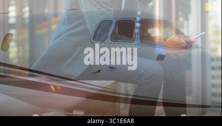 Holding smartphone and stylus, executive in suit leaning on jet wing in hangar, with tinted window Stock Photo