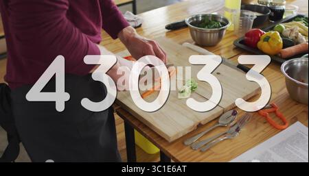 Chopping cook slicing carrots on wood cutting board at kitchen counter wearing apron, copy space Stock Photo