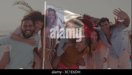 Posing group of friends giving piggyback rides on sandy shore, with flagpole and tiki torches Stock Photo