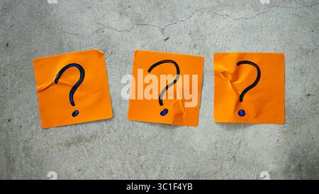 Three Blue Question Marks on Orange Sticky Notes on a Cracked Concrete Background Stock Photo