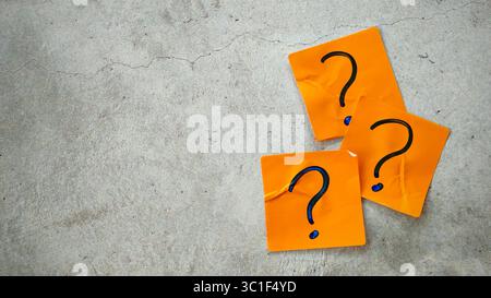 Three Blue Question Marks on Orange Sticky Notes on a Cracked Concrete Background Stock Photo