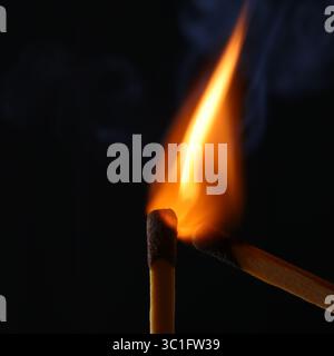 Close-up of burning matchsticks with bright flame against a dark black background. Stock Photo