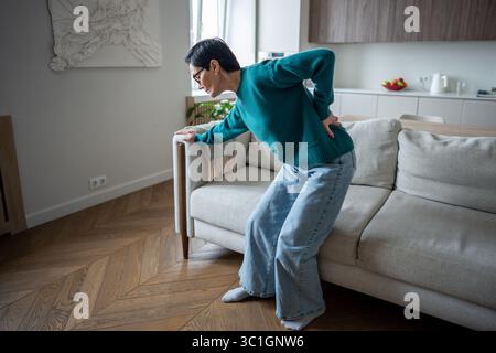 Mature woman clutching back in agony from sudden spinal pain. Herniated disc, joint disease Stock Photo