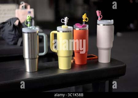 Four colorful insulated tumblers or travel mugs with cute straw toppers lined up on a bench in a gym. Concept of hydration, fitness, and lifestyle. Stock Photo