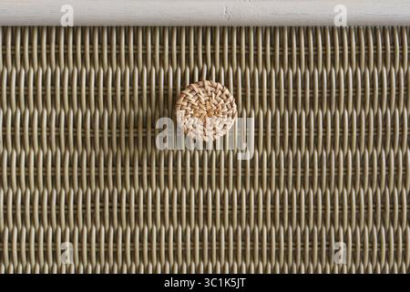 Macro detail of a woven rattan knob on a textured furniture surface. Abstract background of natural, handmade craftsmanship and organic materials. Stock Photo