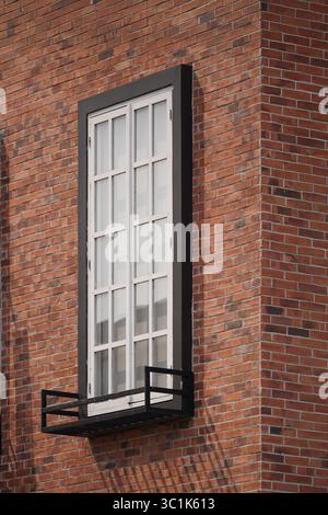 A tall classic white window with a black frame set in a red brick wall. Minimalist architectural detail of a building facade with a clean pattern. Stock Photo